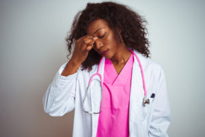 African american doctor woman wearing pink stethoscope over isolated white background tired rubbing nose and eyes feeling fatigue and headache. Stress and frustration concept.