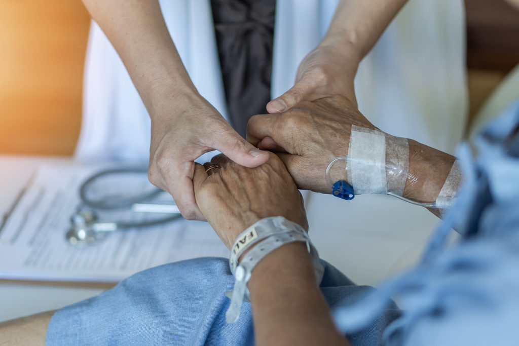 Elderly senior aged patient on bed with geriatric doctor holding hands for trust and nursing health care, medical treatment, caregiver and in-patient ward healthcare in hospital